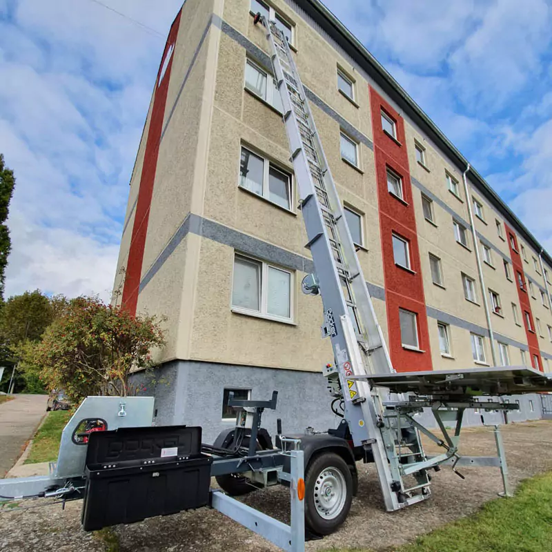 eine Leiter mit einem Möbellift lehnt an der Wand eines Hochhauses