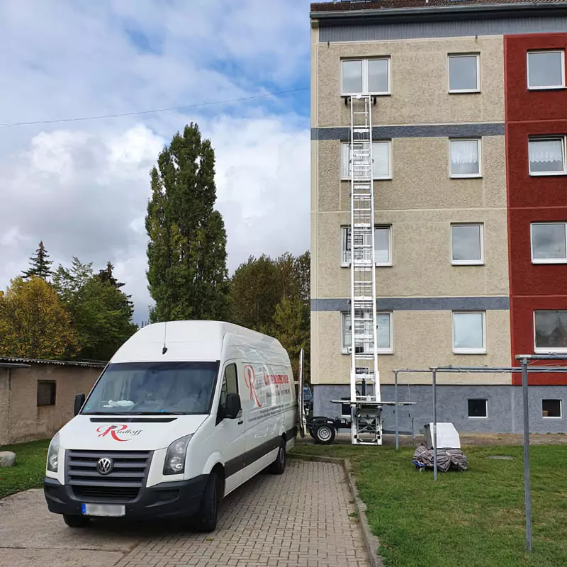 Umzugstransporter / -sprinter steht vor einem mehrstöckigen Wohnhaus an dem eine Leiter für den Möbellift steht